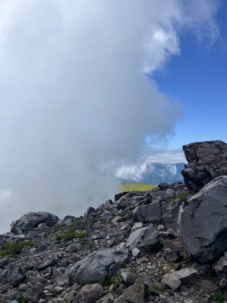 茶臼岳山頂。ガスに覆われ視界が遮られている。奥にはガスがかかっていない箇所があり、緑が美しい。
